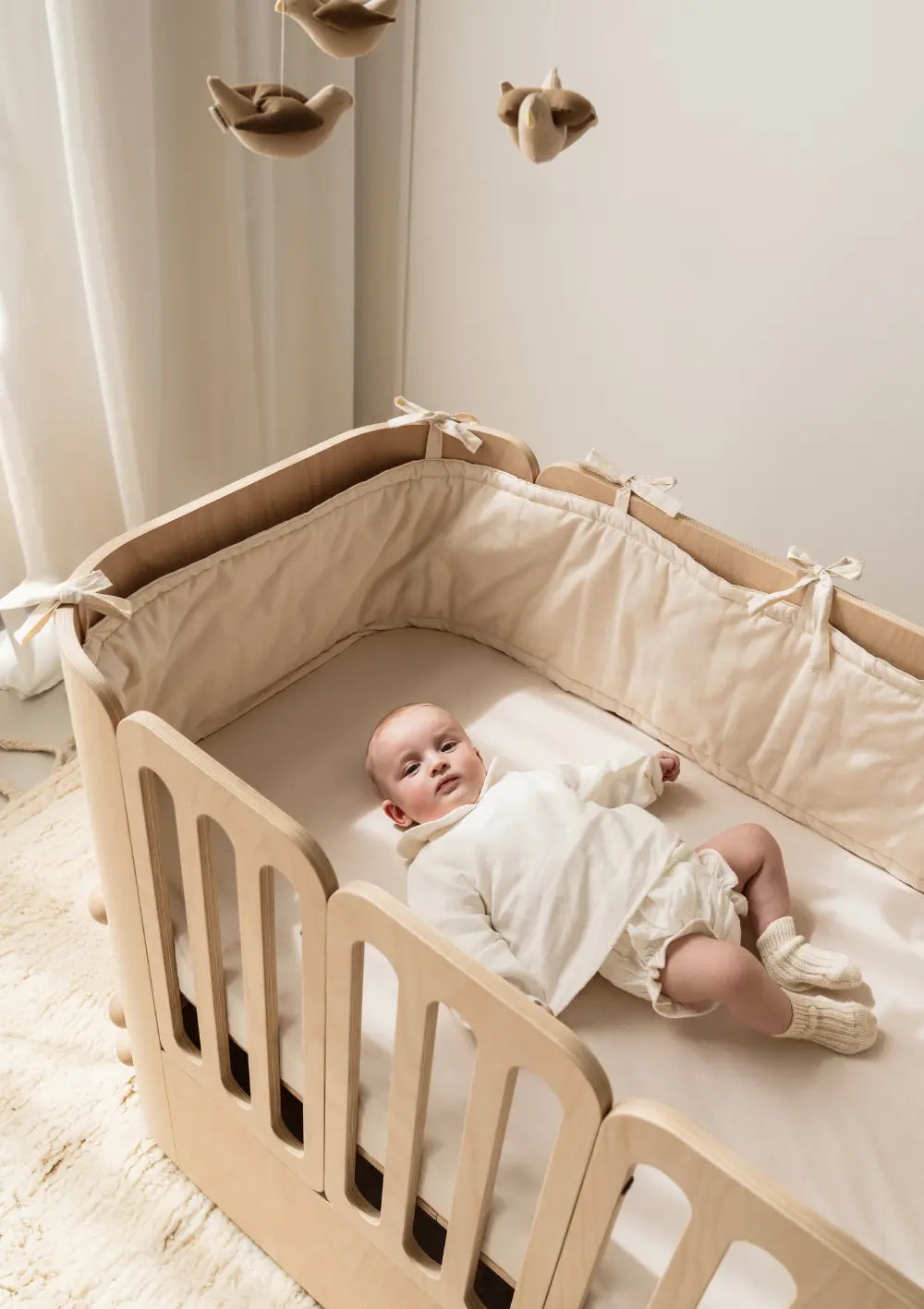 Baby liegt in Nani Berlin 4-in-1 Babybett – ausgestattet mit Nässeschutzauflage 'Nani Berlin x Sproutling'