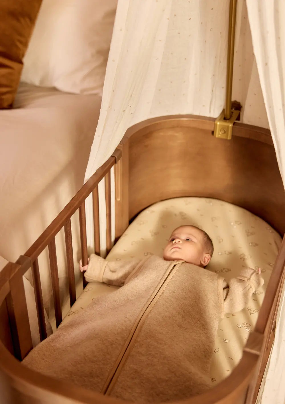 Ein im Bett liegendes Baby trägt den Jollein Merino Baby Schlafsack mit abnehmbaren Ärmeln TOG 2,0-2,5 Natural