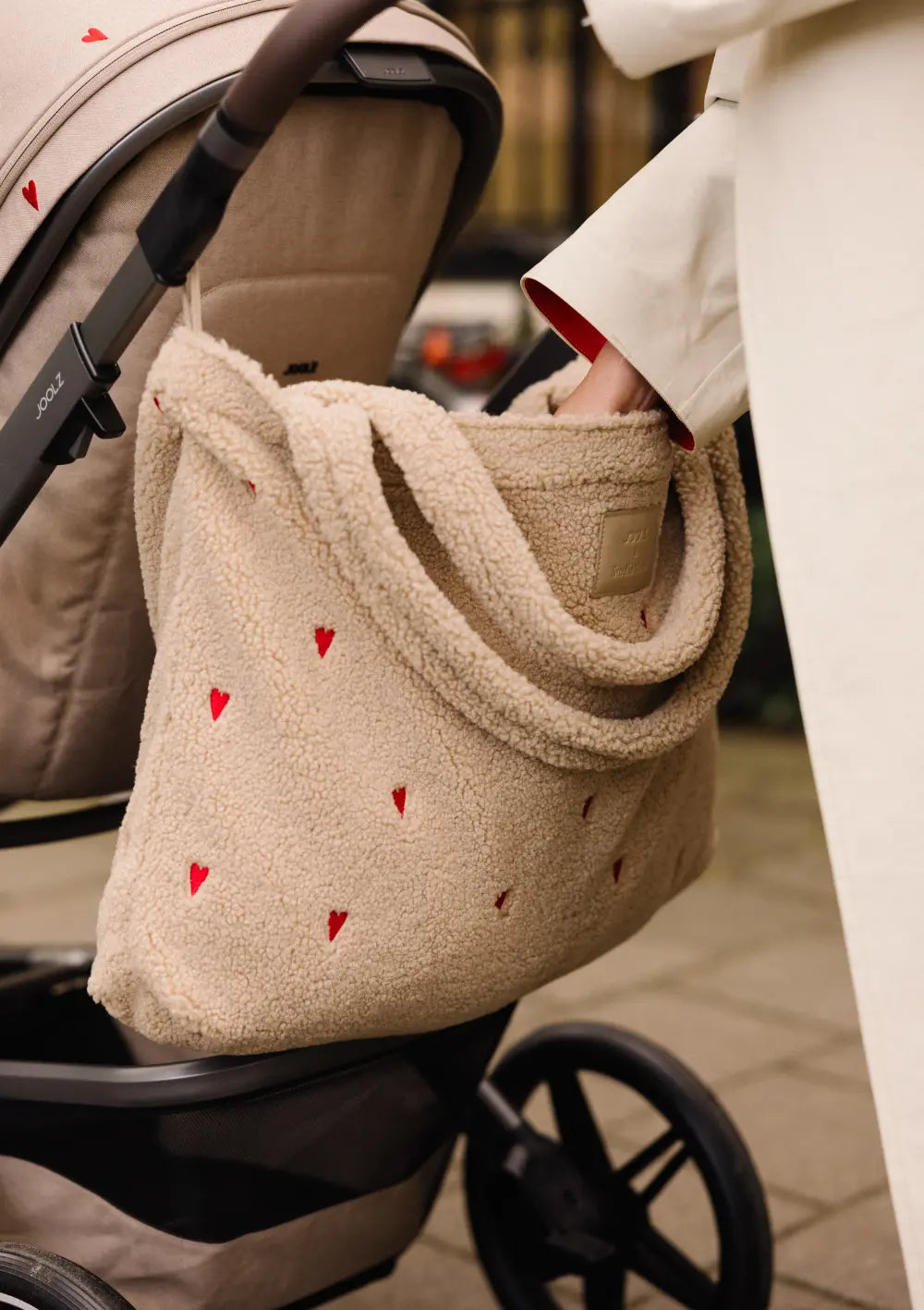 Detailansicht der Teddy-Wickeltasche mit gestickten Herzen am Lenker des Joolz Kinderwagen-Set Day5 x Studio Noos Sandy Taupe, während eine Hand hineingreift.