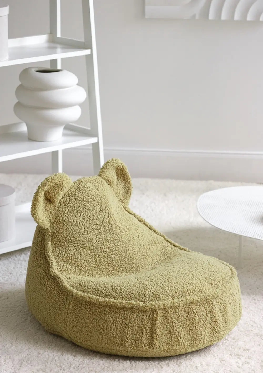 Der pistaziengrüne Wigiwama Bären Sitzsack Teddy Matcha aus flauschigem Teddy-Plüsch mit niedlichen Bärenohren steht freistehend in einem modern eingerichteten Zimmer.
