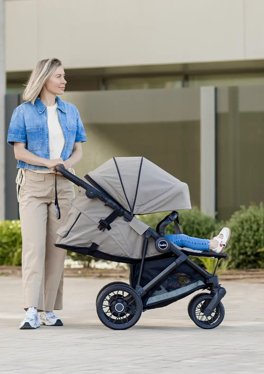 Seitenansicht einer Frau mit dem beigefarbenen Emmaljunga Kinderwagen Sonic Stroller Urban Dune, dessen Sitz in flache Liegeposition gestellt ist.