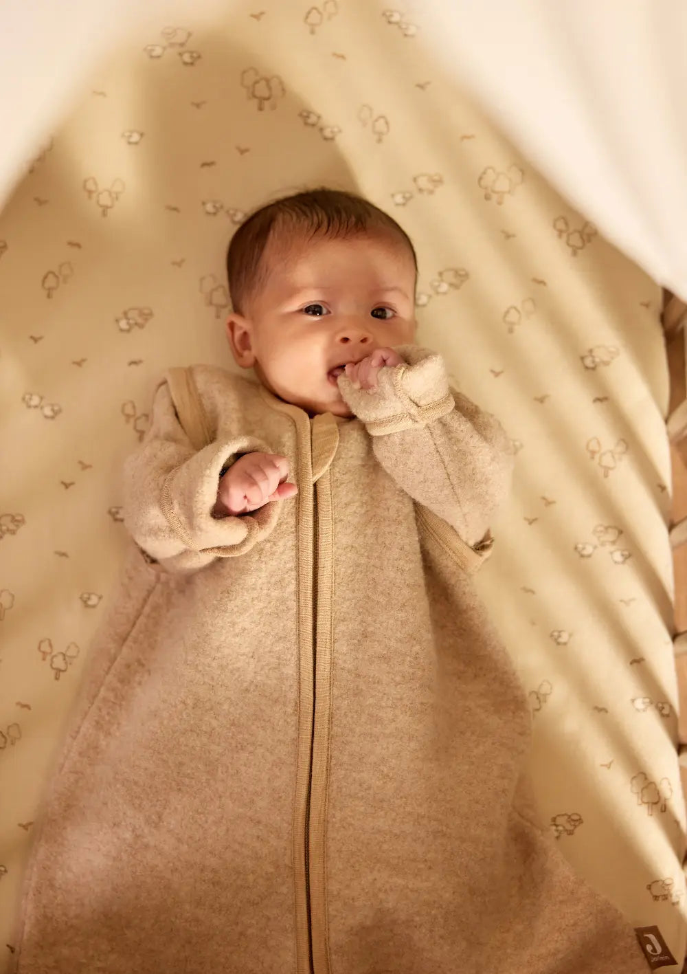 Ein im Bett liegendes Baby trägt den Jollein Merino Baby Schlafsack mit abnehmbaren Ärmeln TOG 2,0-2,5 Natural