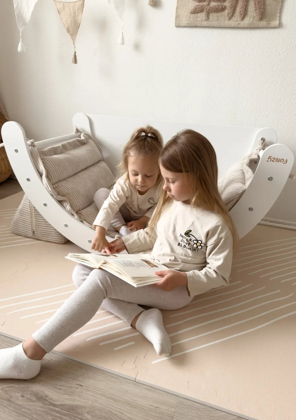 Mädchen beim Lesen; ein Kind sitzt dabei auf dem Funzy Kletterbogen Birke Weiß inkl. Auflage Cord Creme Beige