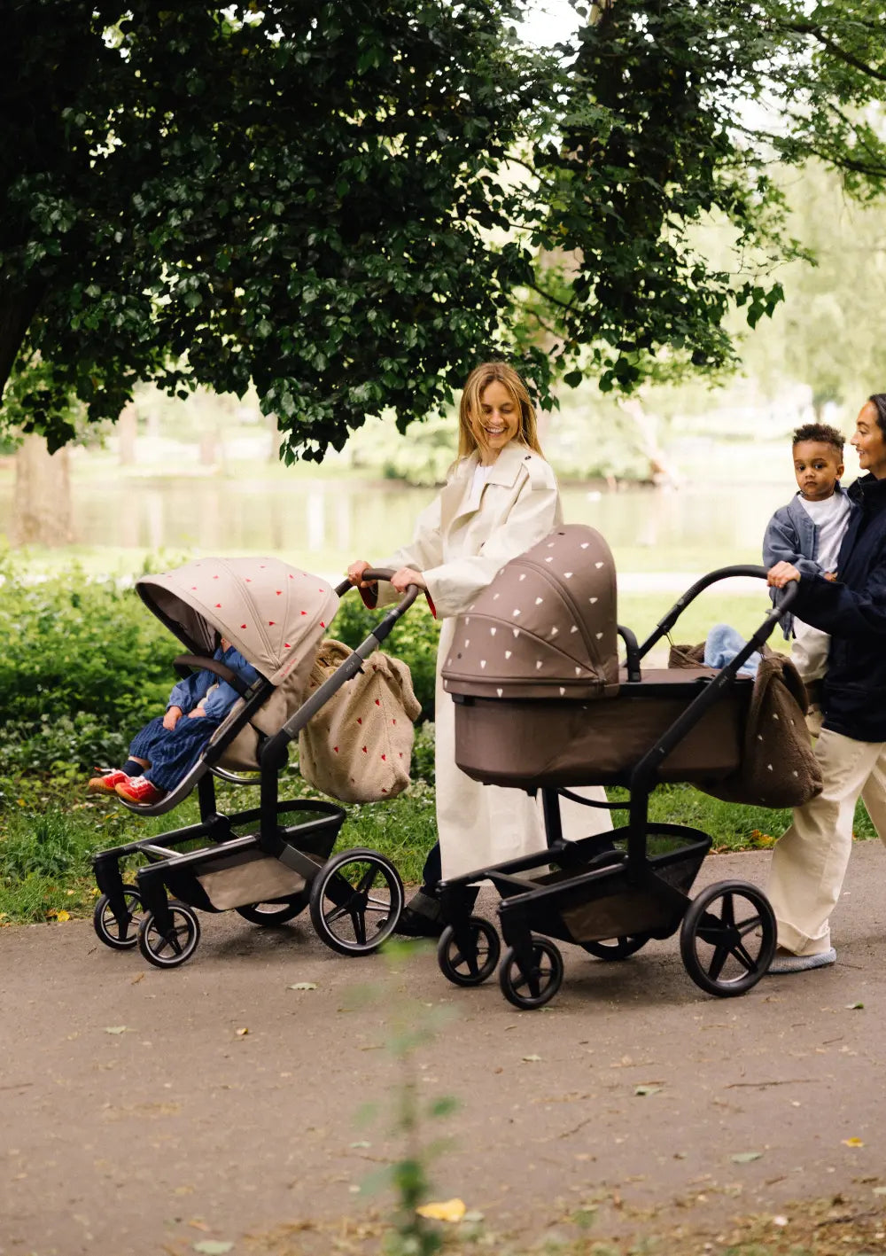Zwei Mütter schieben bei einem Spaziergang im Park den sandfarbenen Buggy und den dunkelbraunen Kombikinderwagen aus der Kollektion Joolz Kinderwagen-Set Day5 x Studio Noos.