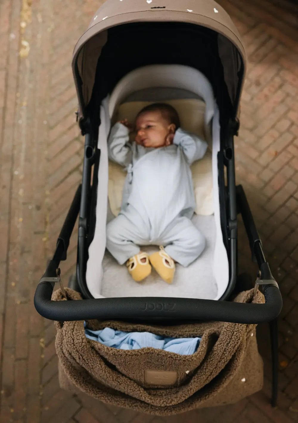 Draufsicht in die Babywanne des Joolz Kinderwagen-Set Day5 x Studio Noos Hazel Brown, in der ein Neugeborenes in einem hellen Strampler geborgen liegt.