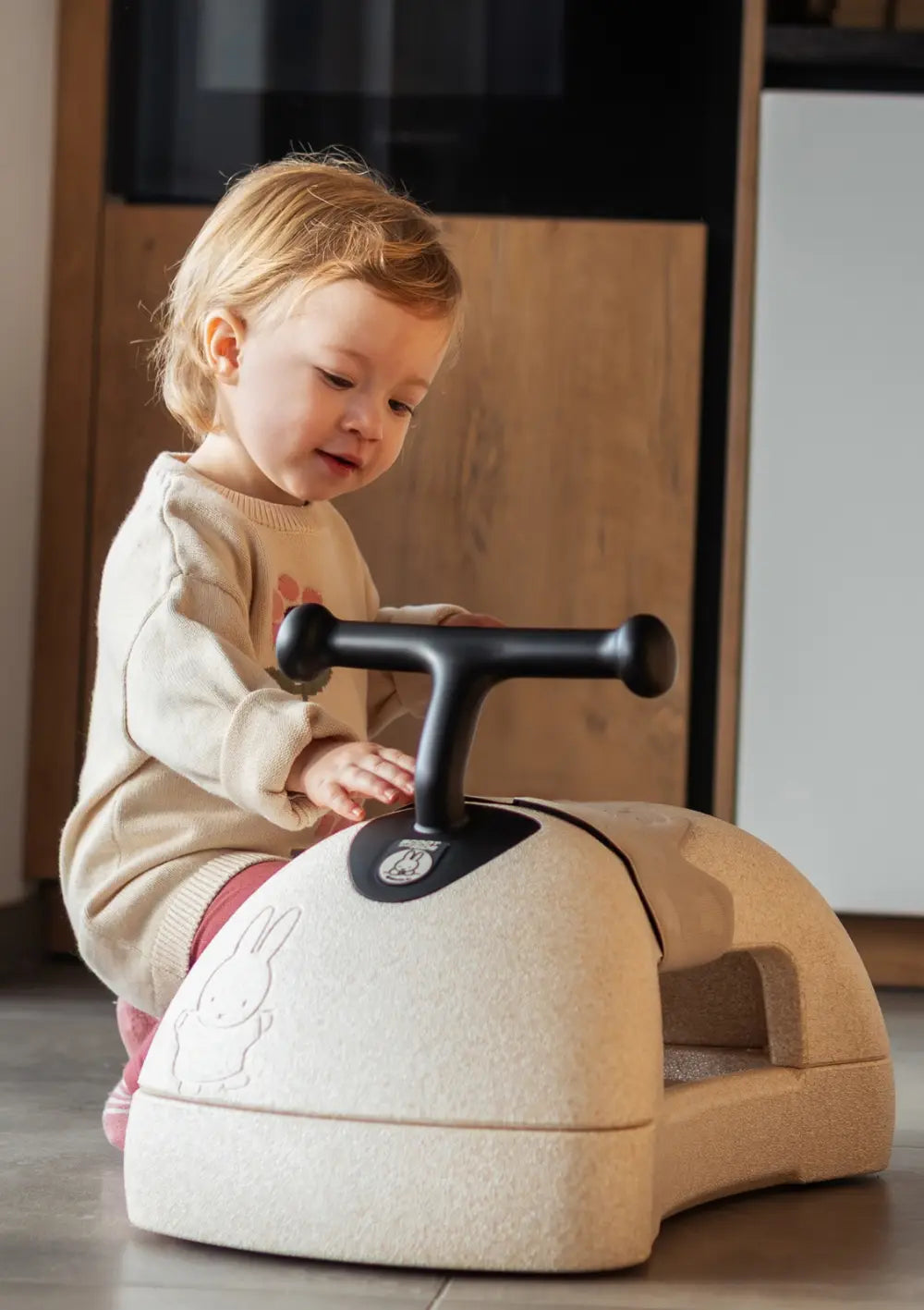 Kind sitzt neben dem Scoot and Ride 3-in-1 Babyroller 'My First' miffy